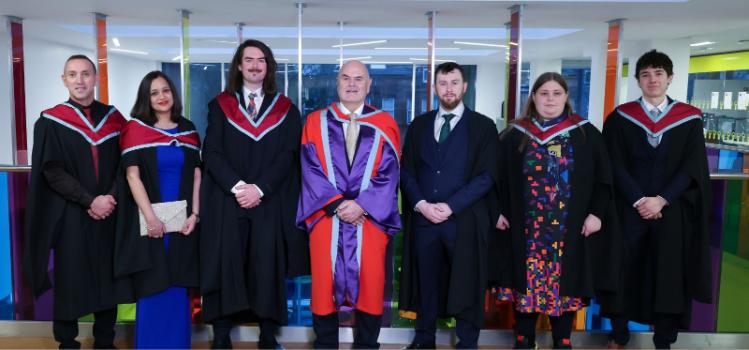 A row of graduates in Master of Science academic costume.
